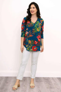 Woman smiling in a blue V-neck floral top with white pants, standing casually