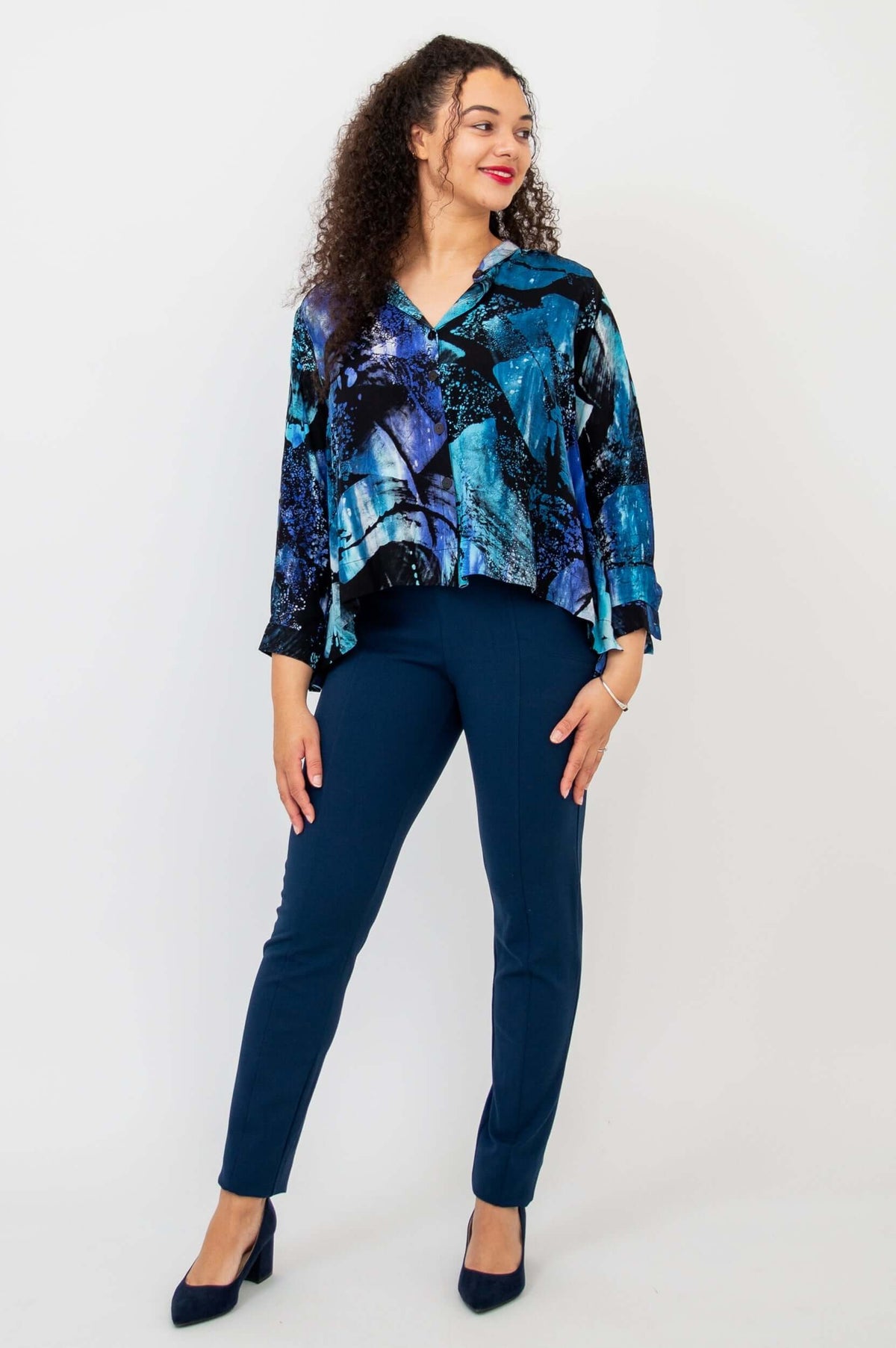 Woman looking to the side, in blue abstract hi-lo blouse and navy pants, full body
