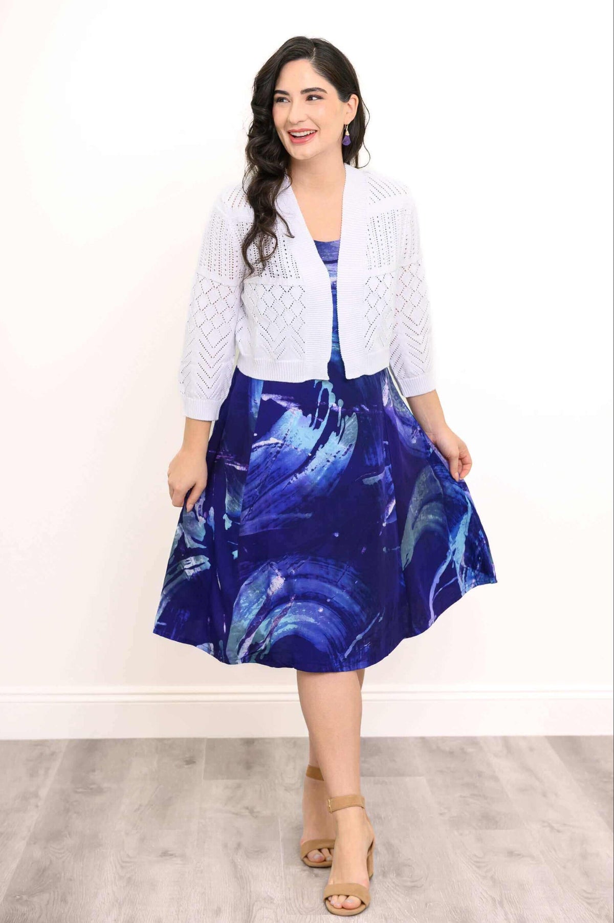 Woman in blue abstract print dress paired with white open-knit cardigan