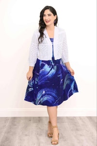 Woman in blue abstract print dress paired with white open-knit cardigan