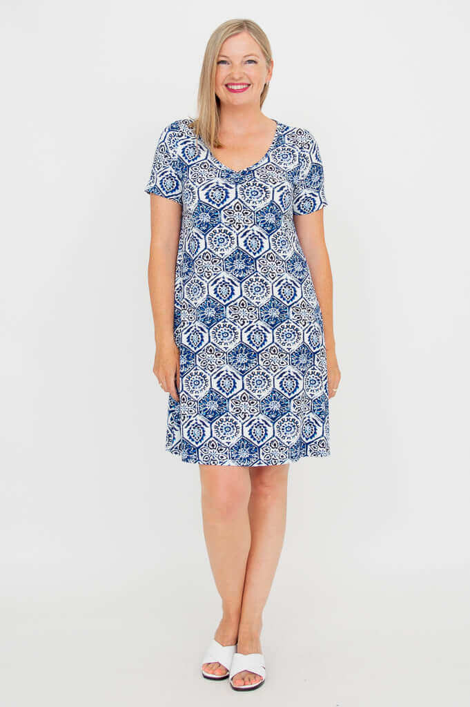 Woman standing in a blue and white short-sleeve patterned dress, smiling, front view