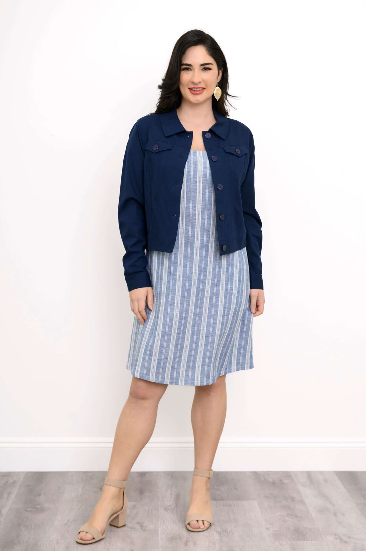 Woman in a blue and white striped shift dress with a navy jacket, facing forward