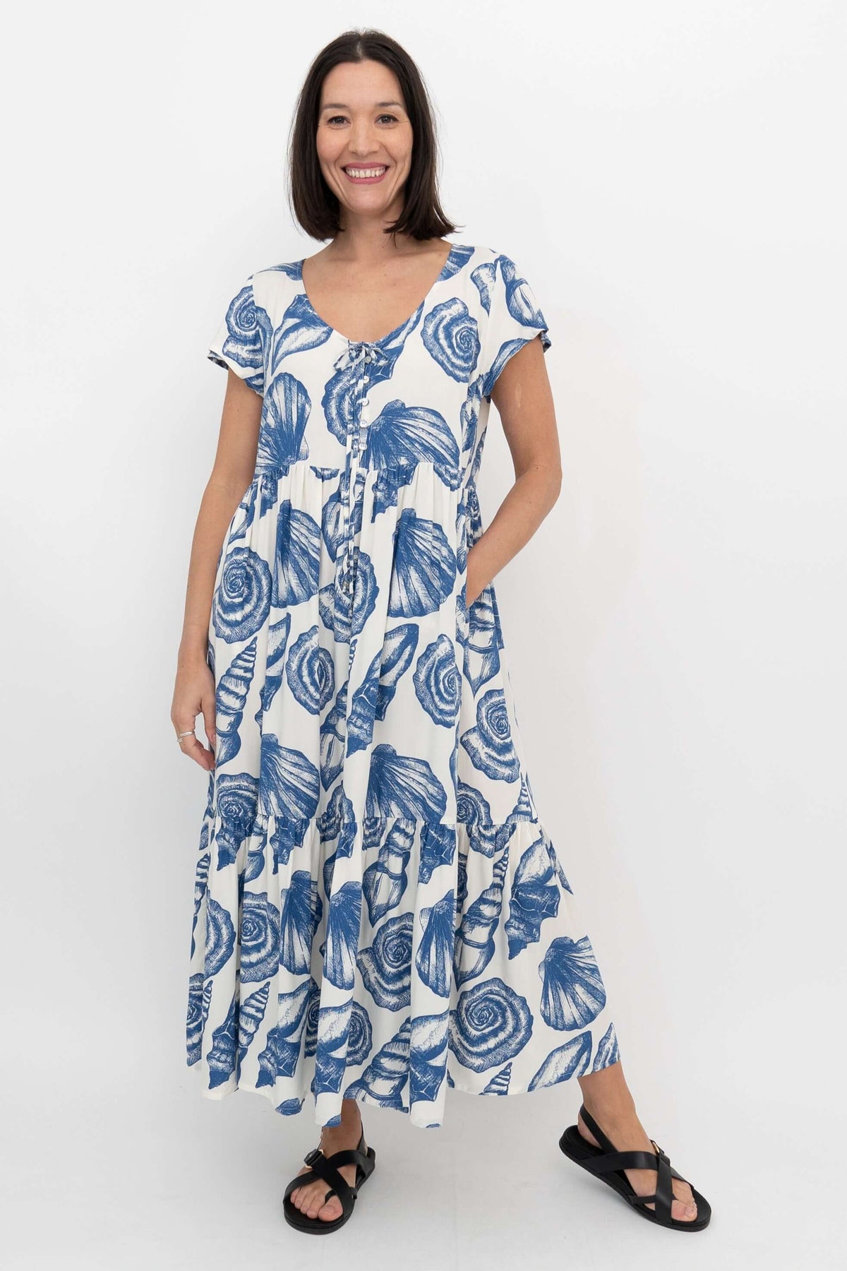 Woman in blue and white tiered seashell dress with pockets, smiling and standing sideways