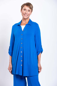Woman smiling in a vibrant blue button-down blouse-jacket with rolled sleeves