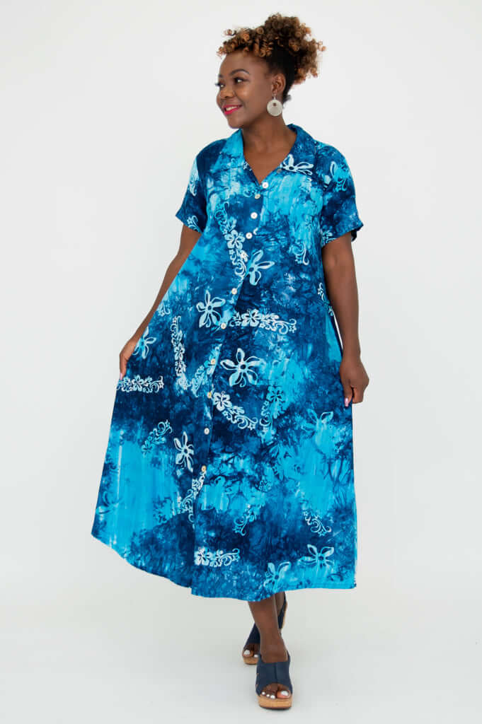Woman in blue batik button-up dress holding skirt, smiling to the side