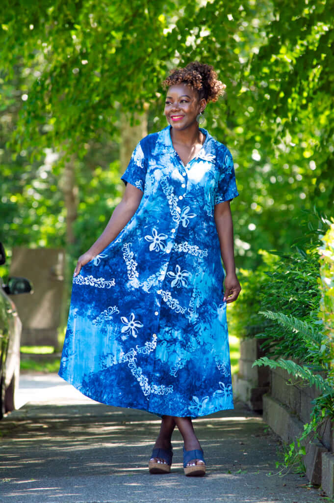Woman in blue batik short sleeve dress standing outside surrounded by greenery