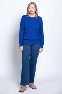 Angled studio view of a woman wearing a bright blue long sleeve crewneck sweater and jeans.