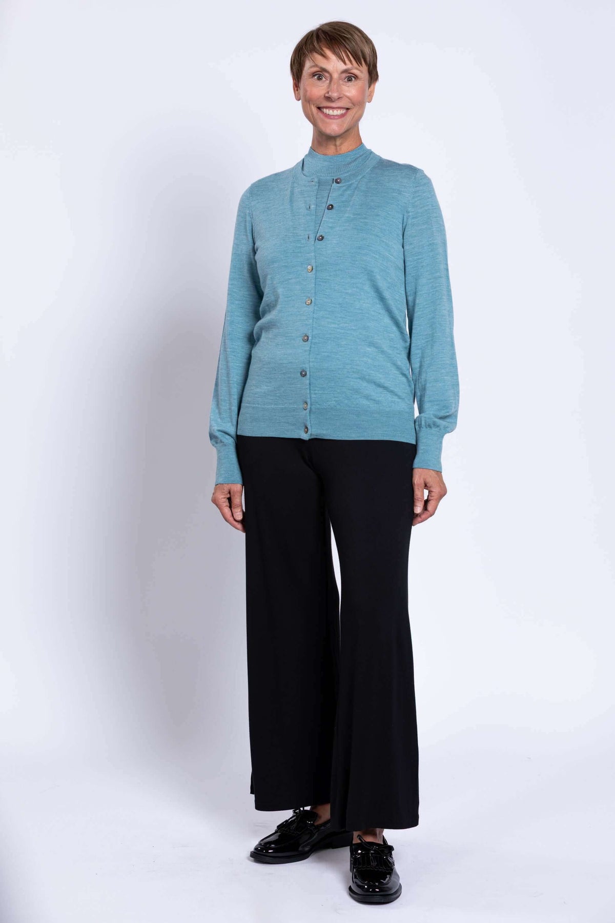 Woman in blue cardigan and black wide-leg pants standing and smiling