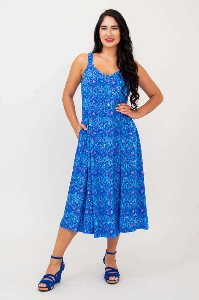 Woman smiling in a blue empire waist midi dress with hands in pockets
