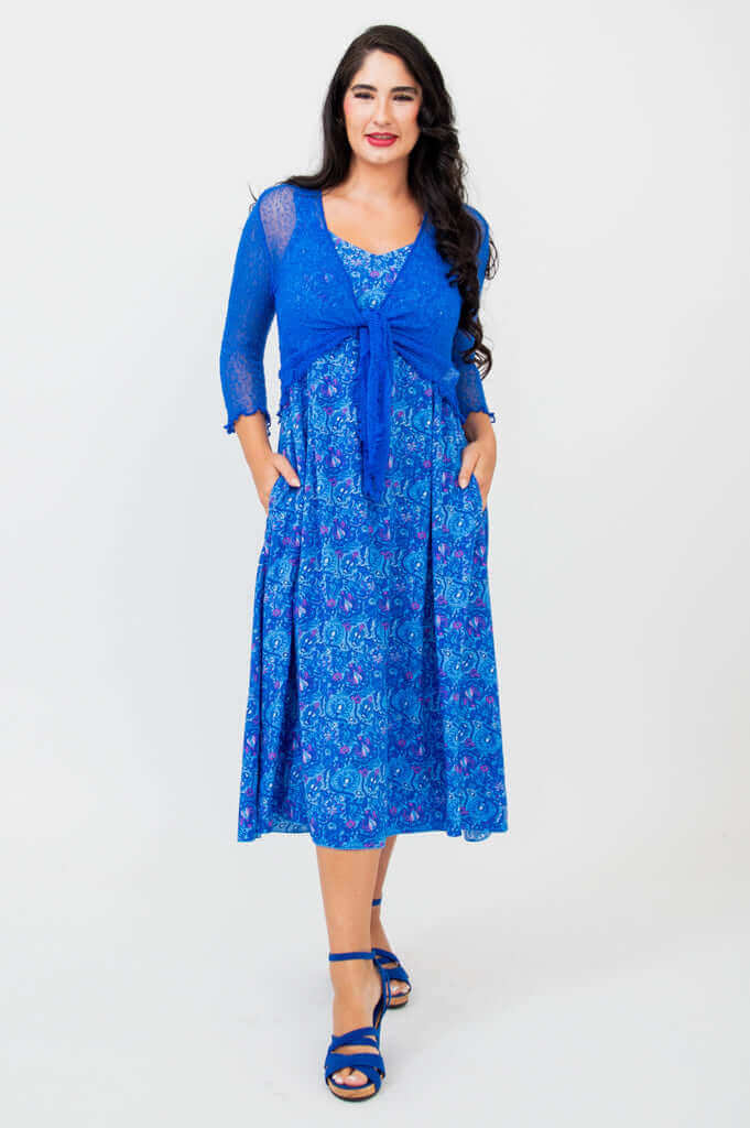 Woman modeling blue empire waist midi dress with lace shrug and pockets
