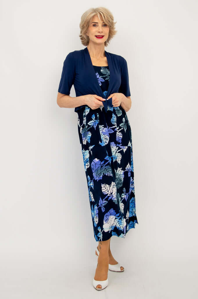 Woman wearing blue floral dress with navy short sleeve shrug, standing confidently