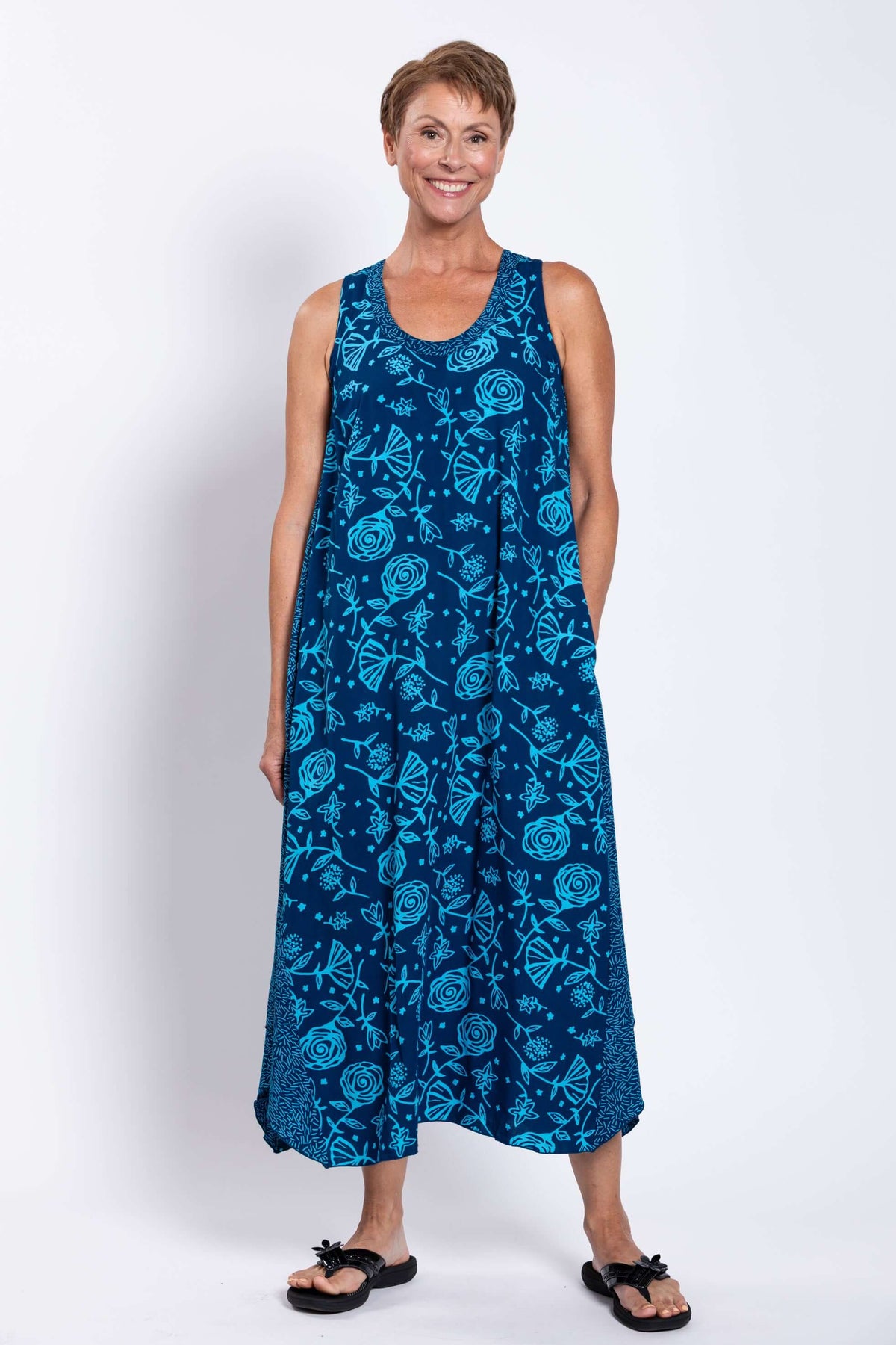 Woman wearing a sleeveless blue midi tank dress with floral print, standing and smiling