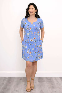 Woman in blue floral shift dress with hands in pockets, wearing tan sandals