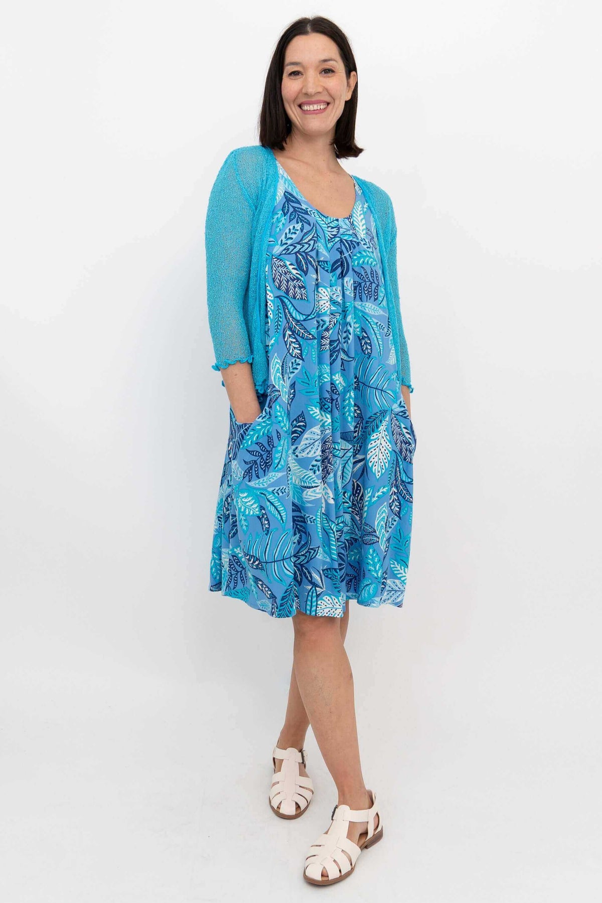 Woman in blue leaf print dress with turquoise cardigan, hands in pockets