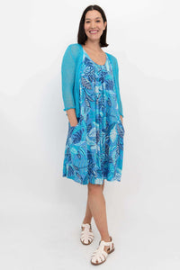 Woman in blue leaf print dress with turquoise cardigan, hands in pockets