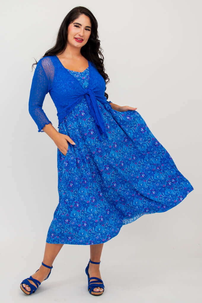 Woman twirling in a blue empire waist midi dress paired with a blue tie-front shrug
