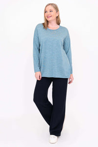 Woman wearing blue pullover sweater, posing with one leg crossed, facing forward
