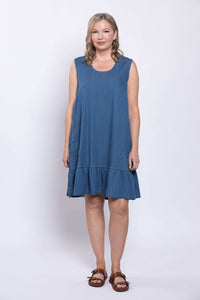 Woman standing straight in a blue sleeveless dress with ruffle hem and pockets