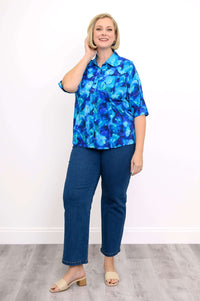 Woman in blue watercolor blouse and jeans, smiling while touching hair