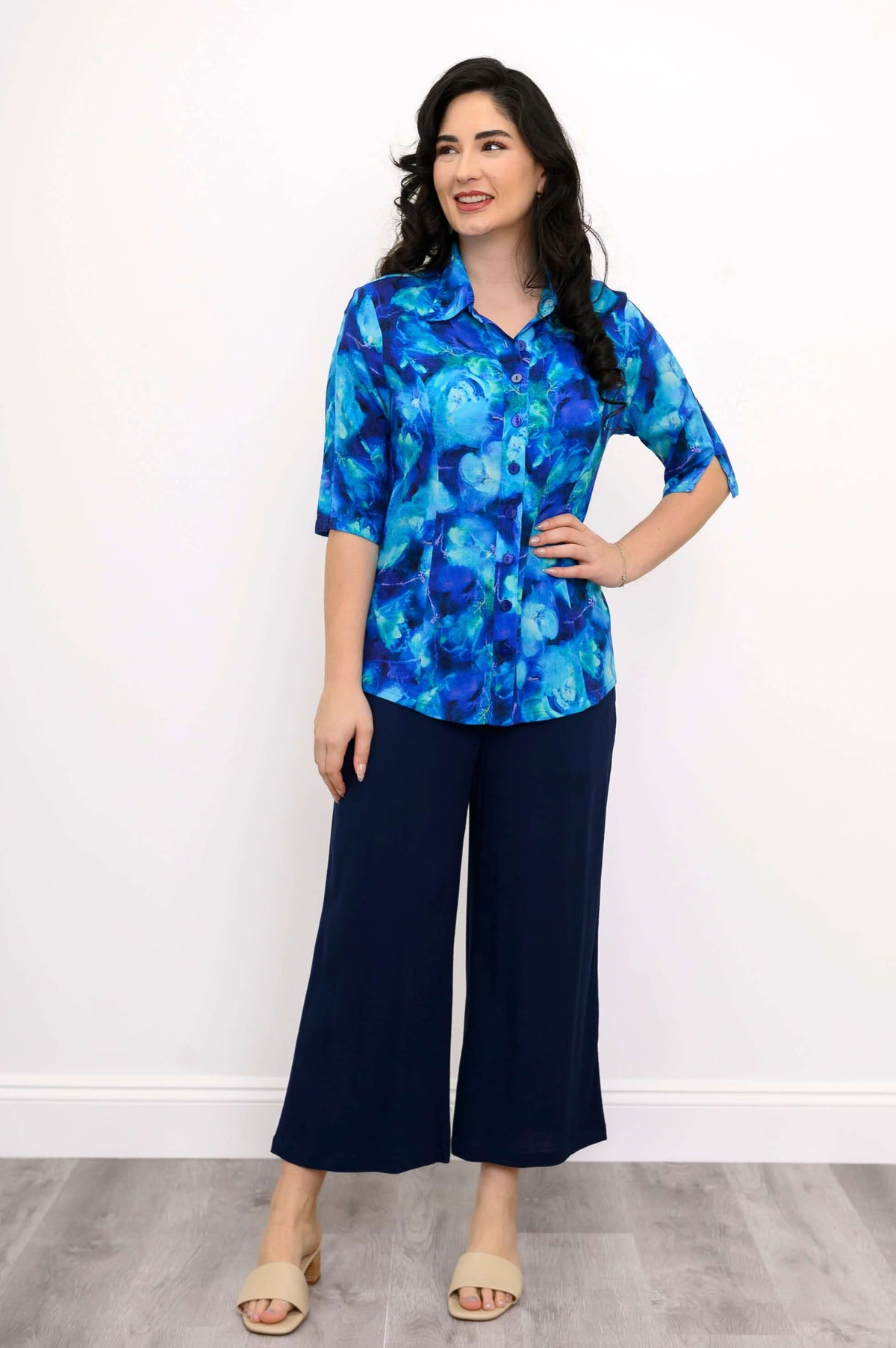 Woman in blue watercolor blouse and navy wide-leg pants, looking to the side