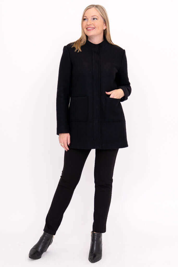 Woman smiling in black boiled wool coat and black pants, posing with hand in pocket