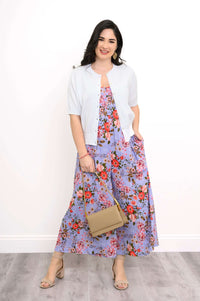 Woman in cardigan and floral jumpsuit holding tan handbag and smiling