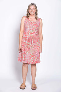 Woman in coral floral print dress, smiling with arms relaxed at her side, front view