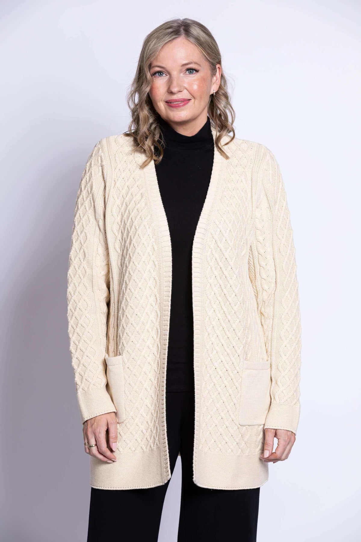 Woman wearing a cream cable knit cardigan with open front and front patch pockets
