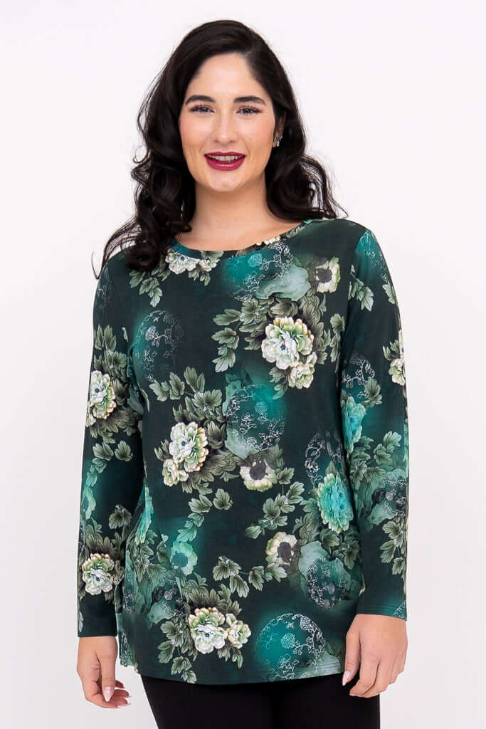Woman in a dark green floral long sleeve tunic top standing and smiling