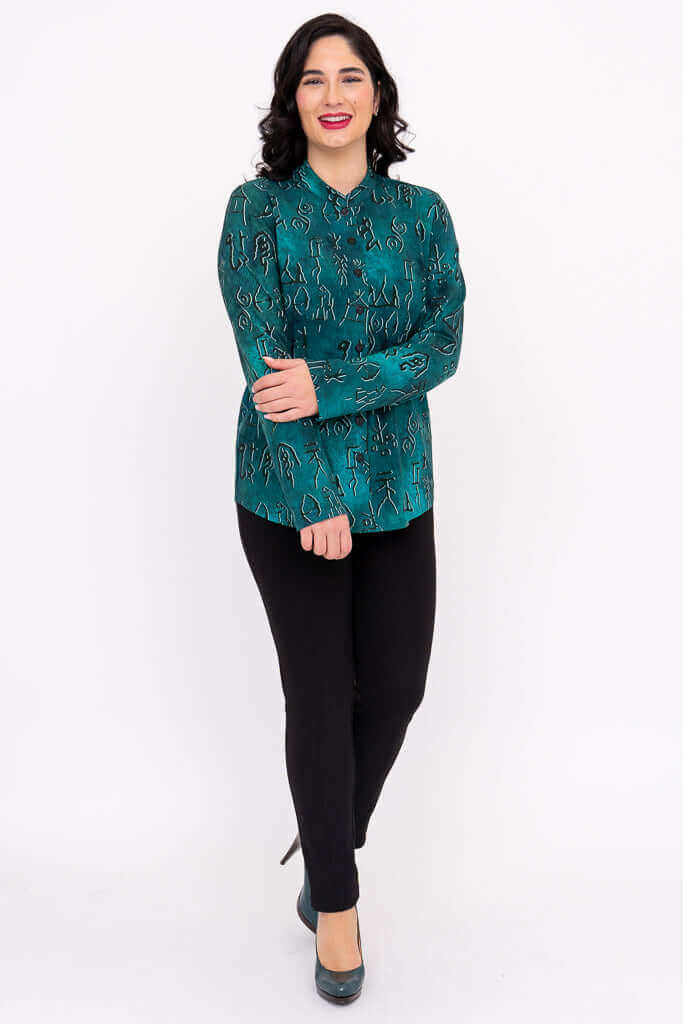 Woman standing with arms crossed in emerald artisan patterned top and black pants