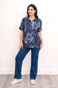 Woman standing in navy floral blouse and blue jeans, casual front view