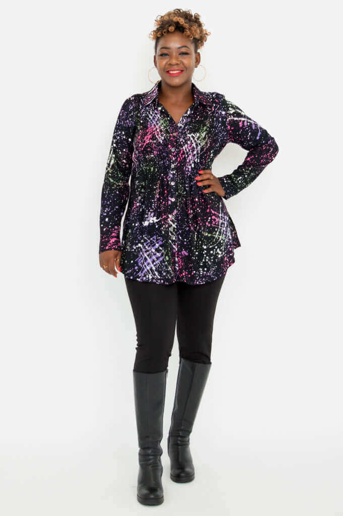 Full body view of a woman in a colorful smocked tunic, black pants, and tall boots