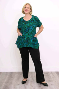 Woman smiling in green and blue print tunic top with hands in side pockets
