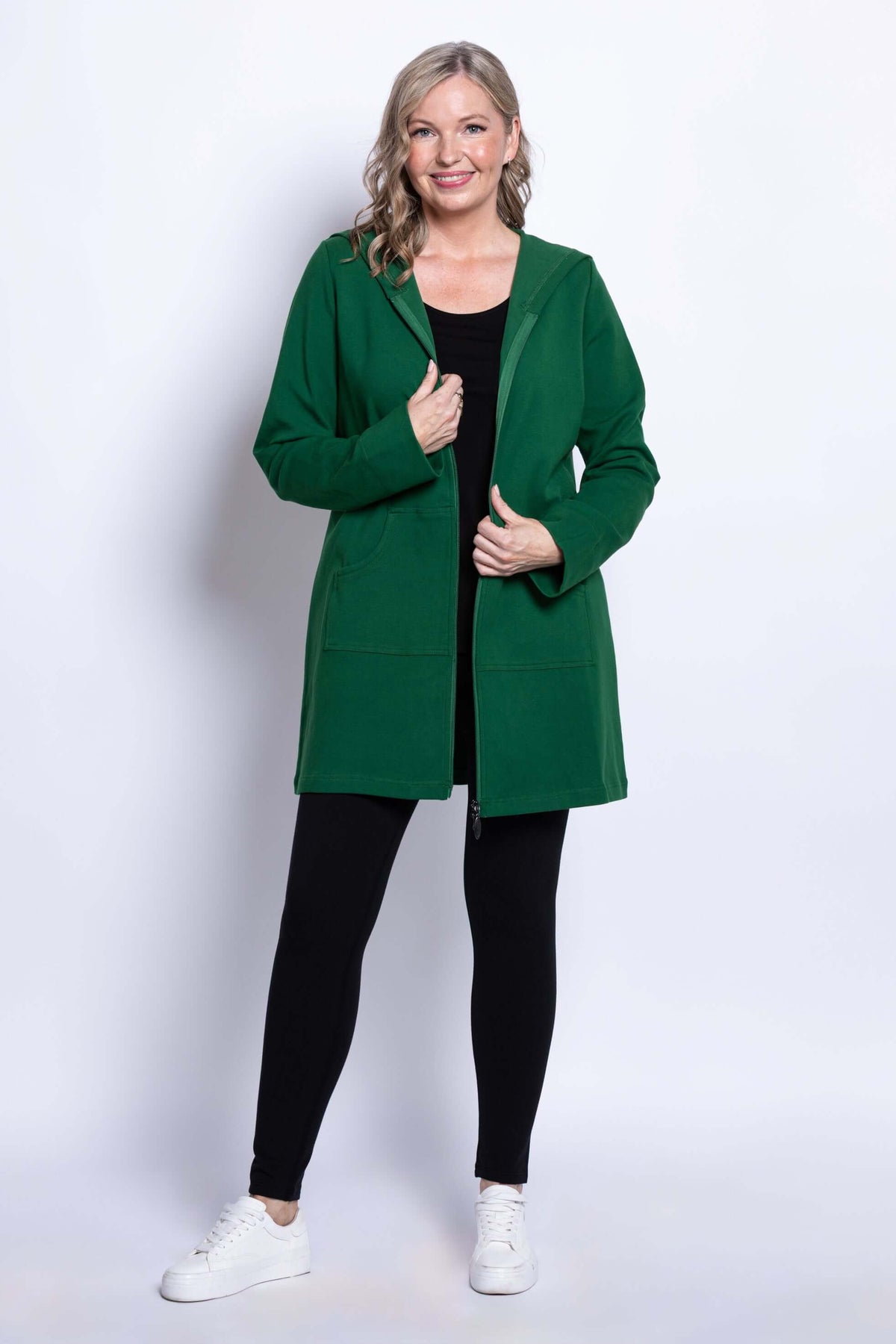 Woman smiling while wearing a green hooded jacket with zipper, black top, and leggings