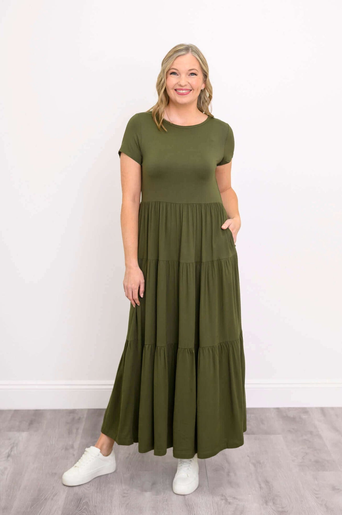 Woman in green maxi dress showing side pocket and smiling