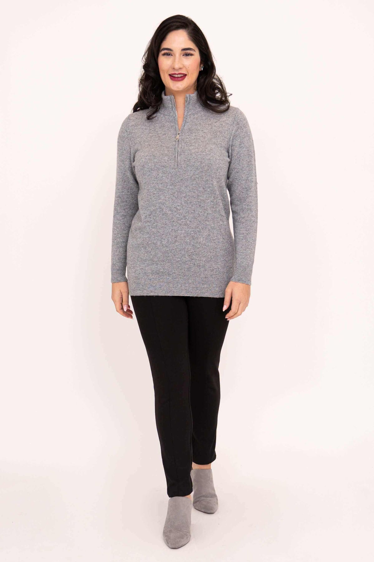 Woman smiling in grey half-zip sweater with black pants and grey shoes