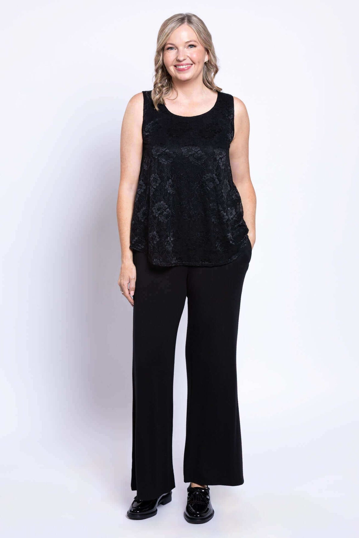 Woman standing and smiling in lace tank top and wide-leg black pants, front view