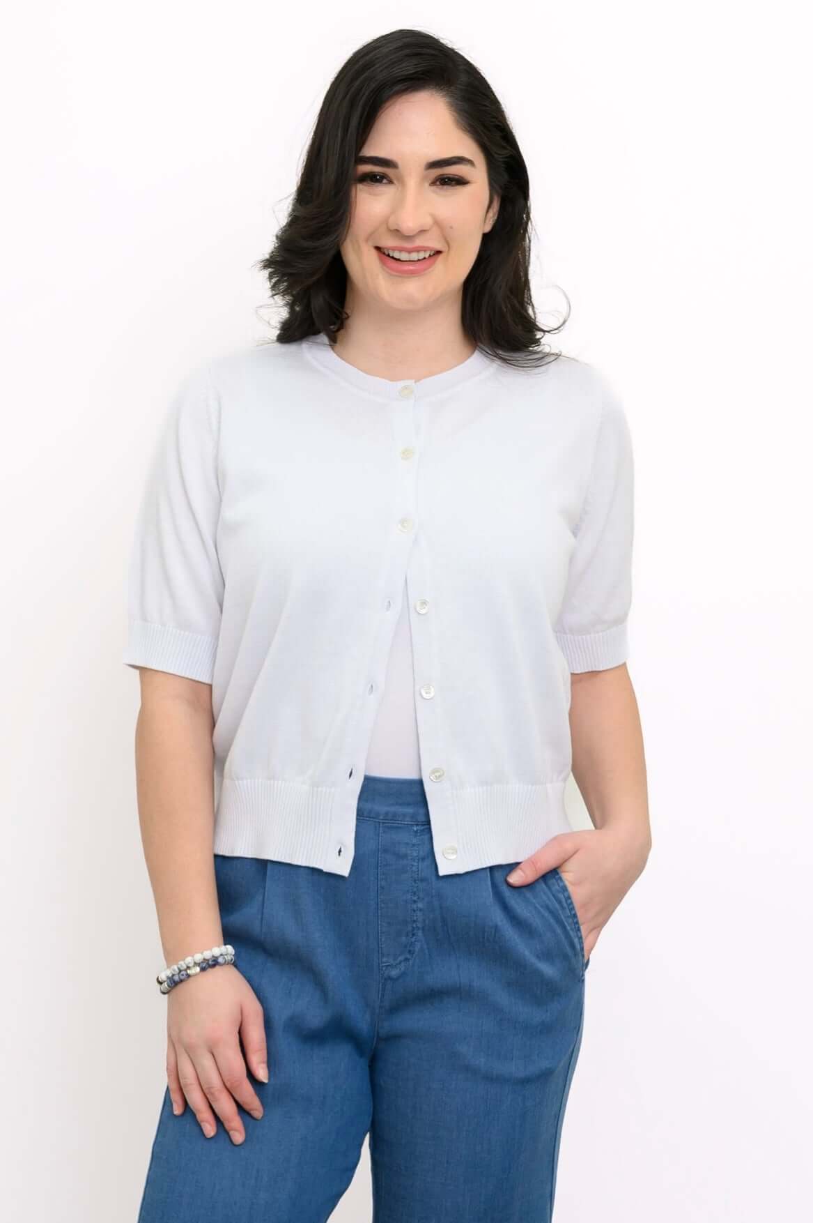 Front view of woman modeling a light short-sleeve buttoned cardigan with blue pants
