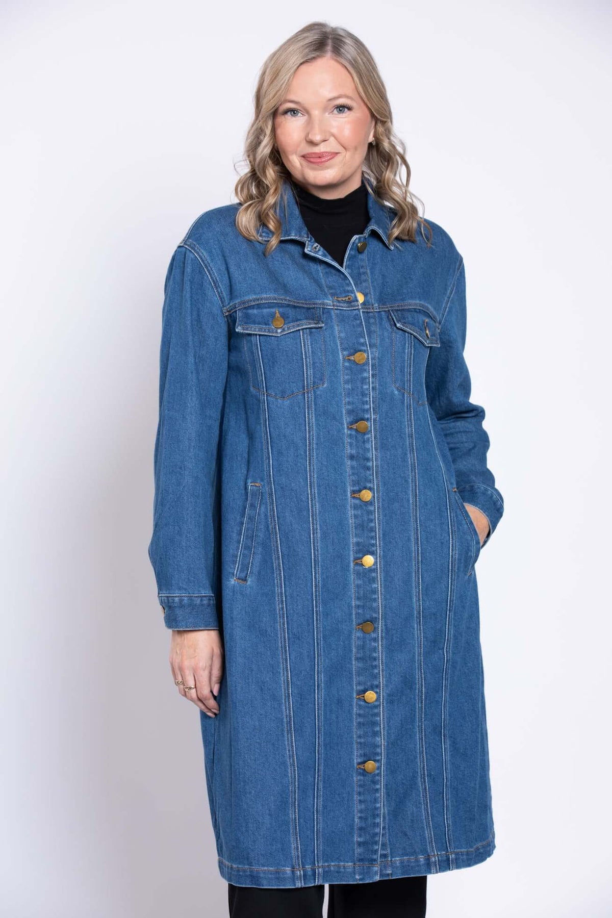 Woman in longline denim jacket with hands in pockets, button details and classic trucker style