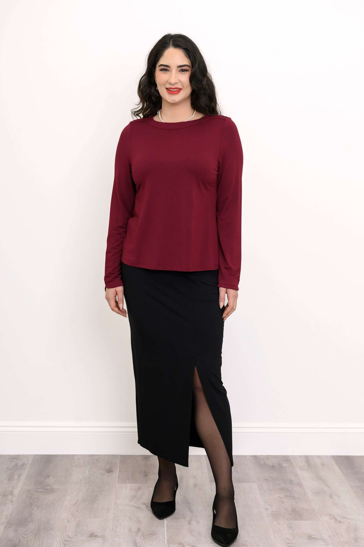 Woman in maroon long sleeve top paired with a black skirt with a front slit