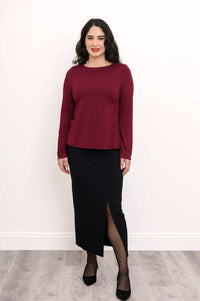 Woman in maroon long sleeve top paired with a black skirt with a front slit