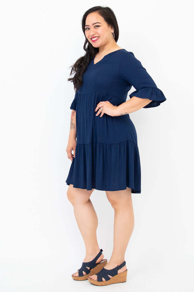Woman in navy dress with empire waist and tiered skirt, shown from the side