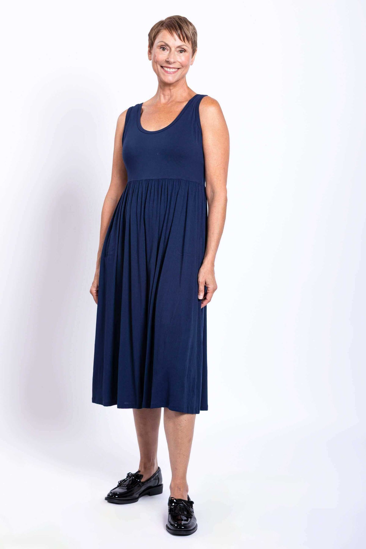 Woman in sleeveless navy empire waist midi dress and black shoes, front view