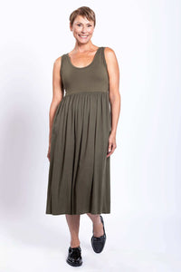 Woman wearing olive empire waist midi dress, taking a step and smiling