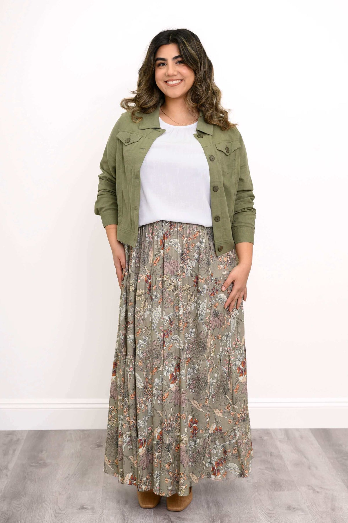 Woman smiling in olive green linen jacket and floral skirt, hands on hips