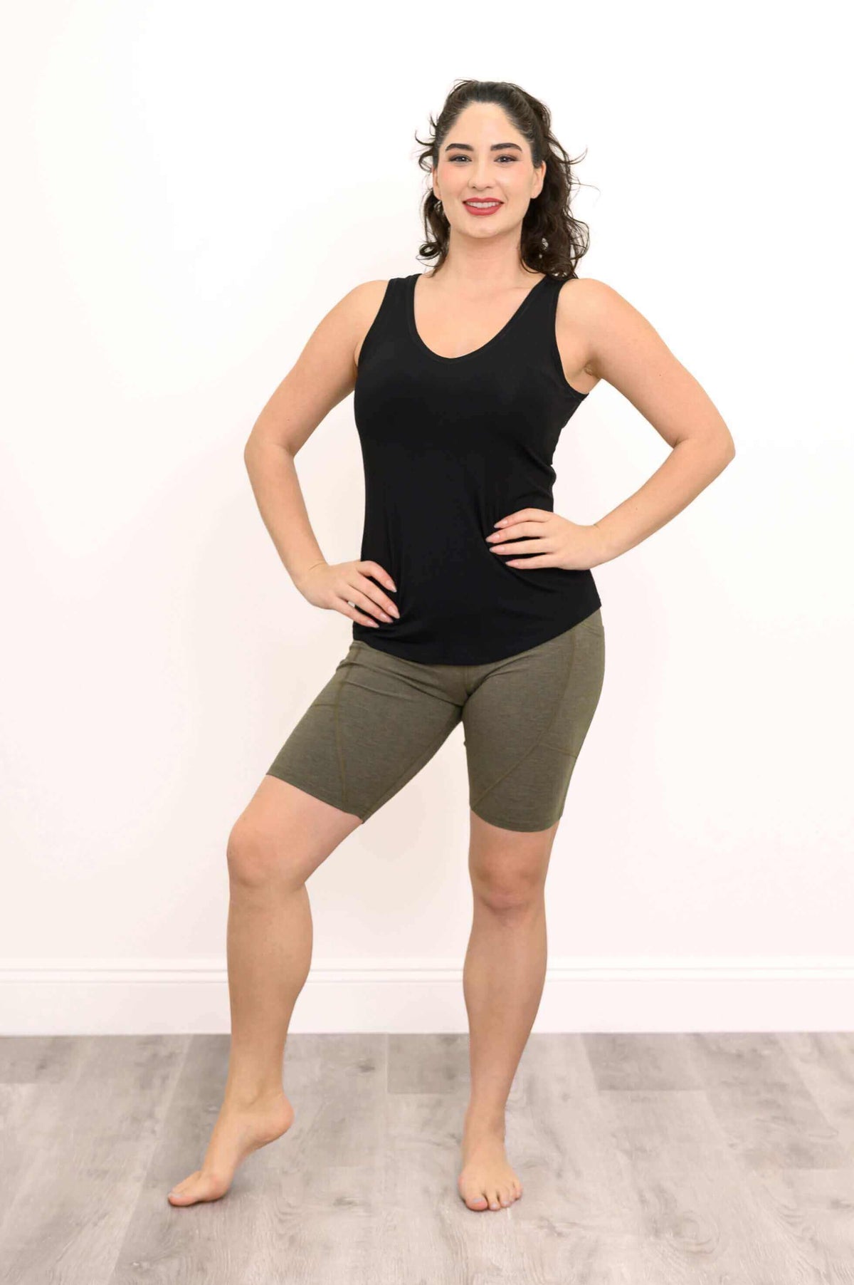 Woman in olive green shorts, hands on hips, standing confidently