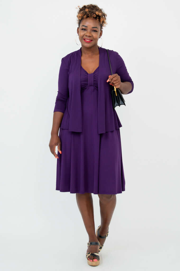 Woman in purple fit and flare dress with matching cardigan, holding a black handbag
