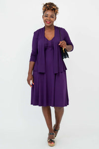 Woman in purple fit and flare dress with matching cardigan, holding a black handbag
