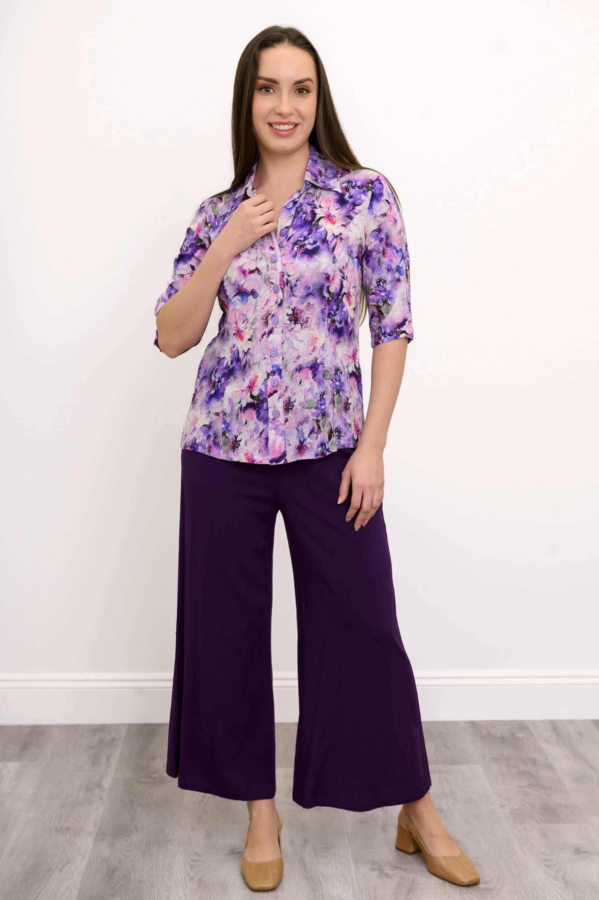 Smiling model in a purple floral blouse paired with wide-leg purple pants, standing