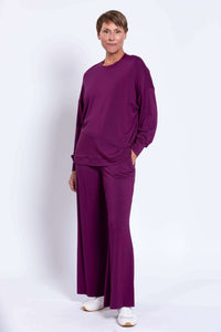 Woman in a relaxed purple crew neck top with hand in pocket, styled with matching pants